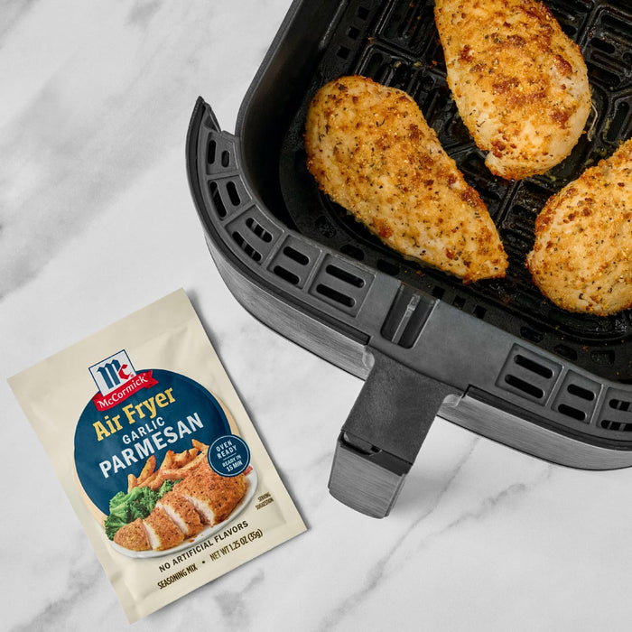 McCormick Air Fryer Parmesan seasoning mix is shown next to an air fryer with cooked chicken breasts inside.