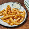 A plate of crispy crinkle-cut fries is served with a creamy dipping sauce.