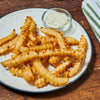 A plate of crispy crinkle-cut fries is served with a creamy dipping sauce.