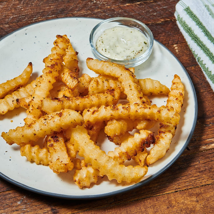 A plate of crispy crinkle-cut fries is served with a creamy dipping sauce.