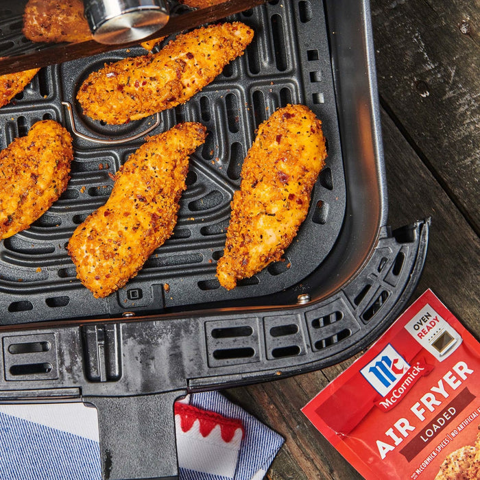 ['McCormick Air Fryer Loaded seasoning packet next to an air fryer with breaded chicken tenders inside.']