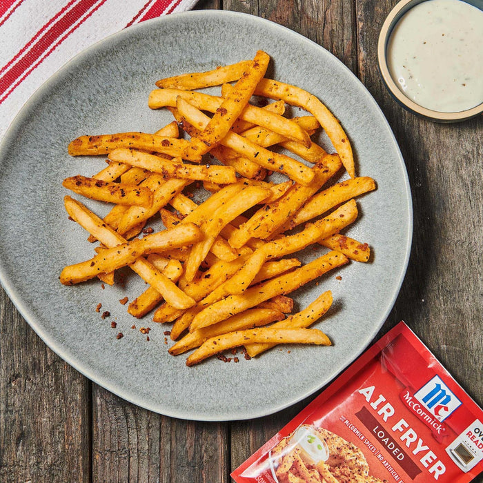 ['A plate of McCormick Air Fryer Loaded seasoned fries with a side of dipping sauce.']