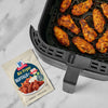 A package of McCormick Air Fryer Hot Buffalo Seasoning Mix sits next to an air fryer basket filled with cooked chicken wings.