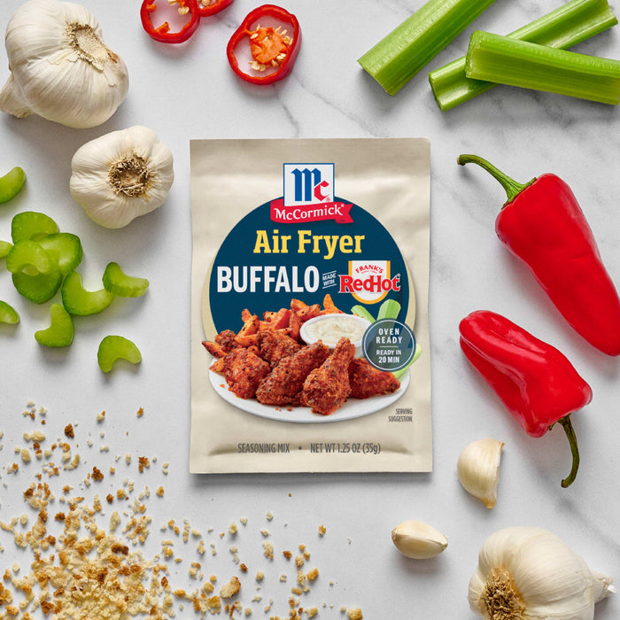 McCormick Air Fryer Buffalo Wings seasoning mix is displayed amidst fresh ingredients like celery, garlic, and peppers.