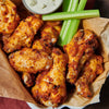A basket of crispy chicken wings served with celery sticks and a creamy dipping sauce.