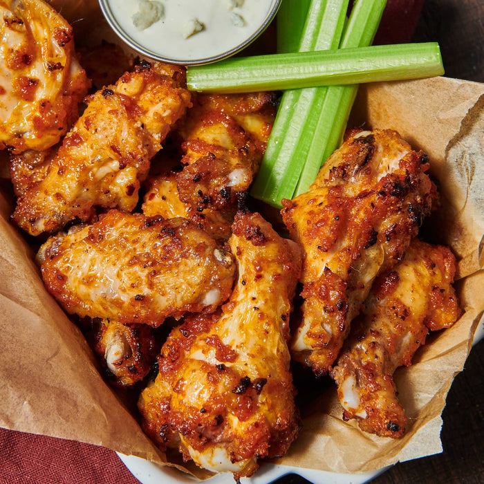 A basket of crispy chicken wings served with celery sticks and a creamy dipping sauce.