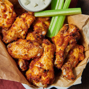 A basket of crispy chicken wings served with celery sticks and a creamy dipping sauce.