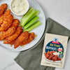 A plate of air-fried buffalo chicken tenders with celery and dipping sauce, alongside a packet of McCormick Air Fryer Buffalo Wings seasoning mix.