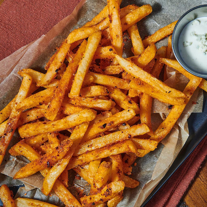 A serving of seasoned french fries is presented with a side of creamy dipping sauce.