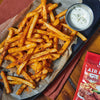 ["A plate of crispy, seasoned french fries with a side of blue cheese dip and a packet of Frank's RedHot seasoning."]