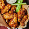 ['A plate of crispy chicken wings with celery sticks and blue cheese dip.']