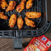 ['A black air fryer basket filled with crispy buffalo chicken wings, next to a McCormick RedHot Air Fryer Buffalo seasoning packet.']