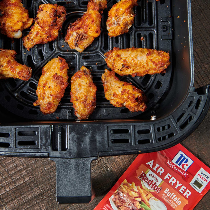 ['A black air fryer basket filled with crispy buffalo chicken wings, next to a McCormick RedHot Air Fryer Buffalo seasoning packet.']