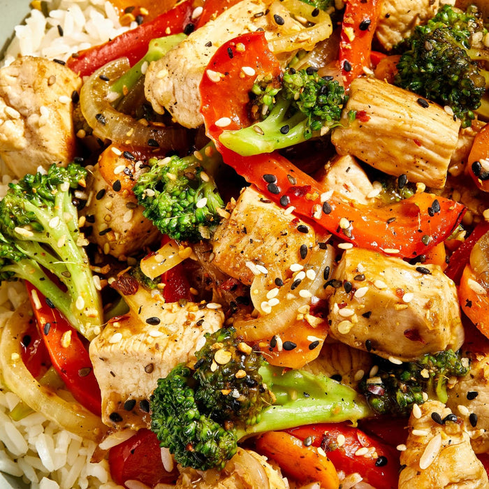 ['A close-up of a plate of chicken stir-fry with broccoli, peppers, and onions.']