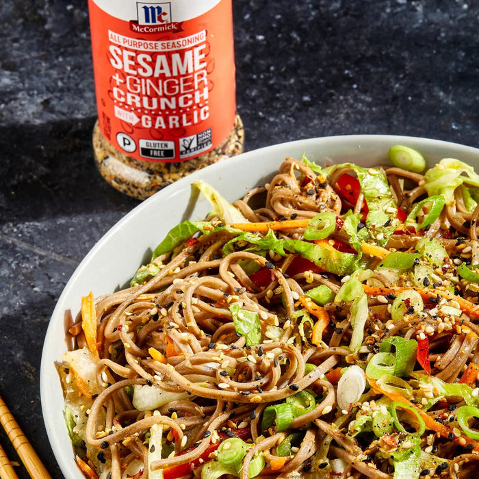 ['A bowl of soba noodles with vegetables and sesame seeds, next to a jar of McCormick Sesame Ginger Crunch Garlic seasoning.']