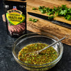 A package of McCormick Grill Mates Brazilian Steakhouse 30 Minute Marinade is next to a bowl of marinade with a whisk a knife and cilantro on a cutting board.