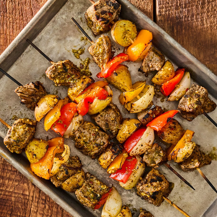 Overhead shot of grilled meat and vegetable skewers on a metal tray showcasing a delicious and colorful meal.