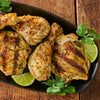 Grilled chicken pieces with lime and cilantro are arranged on a black plate.