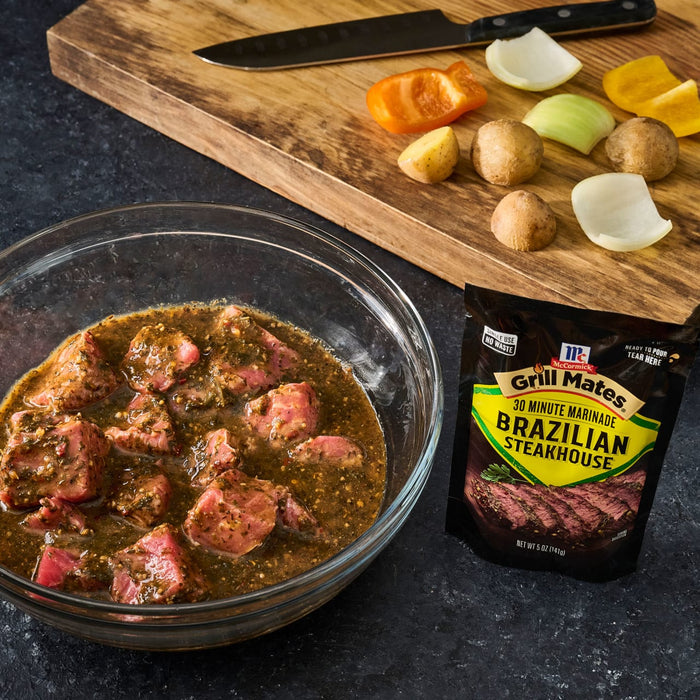 A bowl of marinated steak with McCormick Grill Mates Brazilian Steakhouse marinade packet along with a cutting board with vegetables and a knife.