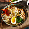 ['A bowl of ramen noodles with chicken, carrots, bean sprouts, spinach, and a soft boiled egg.']