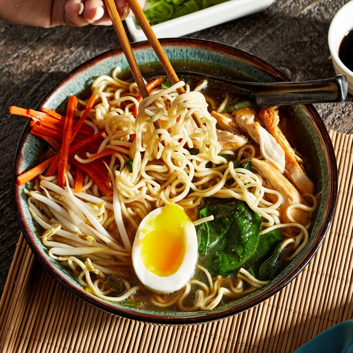 ['A bowl of ramen noodles with chicken, carrots, bean sprouts, spinach, and a soft boiled egg.']