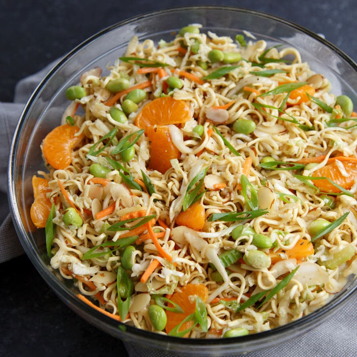 ['A bowl of ramen noodles with mandarin oranges, edamame, and green onions.']