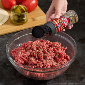 A person seasons ground beef in a glass bowl with McCormick Montreal Steak Seasoning.