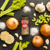 A bottle of McCormick Smash seasoning is surrounded by fresh ingredients like onions, garlic, celery, and salt.