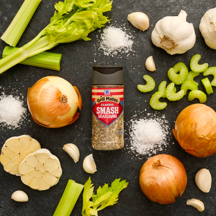 A bottle of McCormick Smash seasoning is surrounded by fresh ingredients like onions, garlic, celery, and salt.
