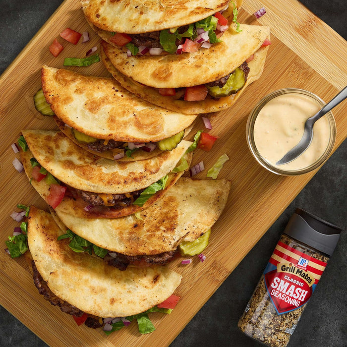 A wooden board displays stacked Jack's Famous Smash Tacos with a side of dipping sauce and a bottle of Jack's Famous Smash seasoning.