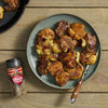 A plate of smashed potatoes seasoned with McCormick's Savory Spice Blend sits next to the spice container on a wooden table.