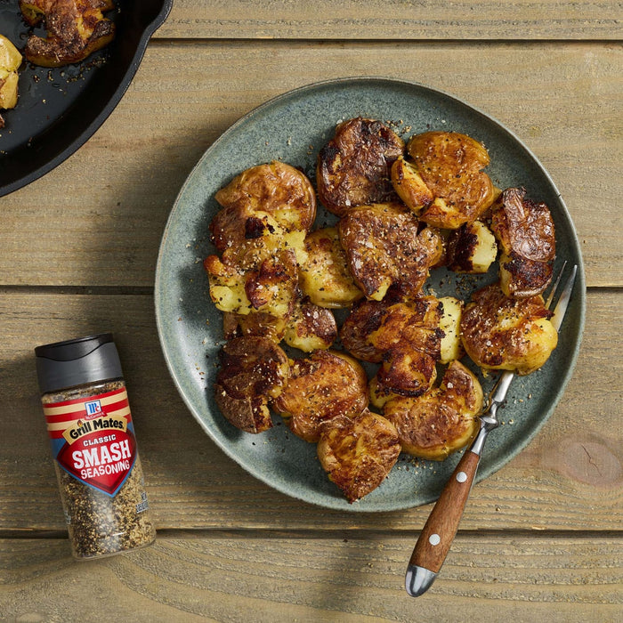 A plate of smashed potatoes seasoned with McCormick's Savory Spice Blend sits next to the spice container on a wooden table.