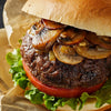 A close-up of a juicy burger topped with sauteed mushrooms and onions.