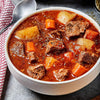 A bowl of beef stew with potatoes, carrots, and herbs.