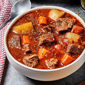 A bowl of beef stew with potatoes, carrots, and herbs.