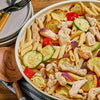 A bowl of pasta with chicken, zucchini, and squash.