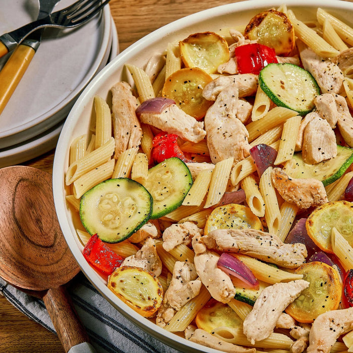 A bowl of pasta with chicken, zucchini, and squash.