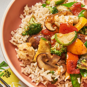 ['A bowl of brown rice with stir-fried vegetables and mushrooms.']