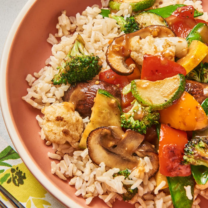 ['A bowl of brown rice with stir-fried vegetables and mushrooms.']
