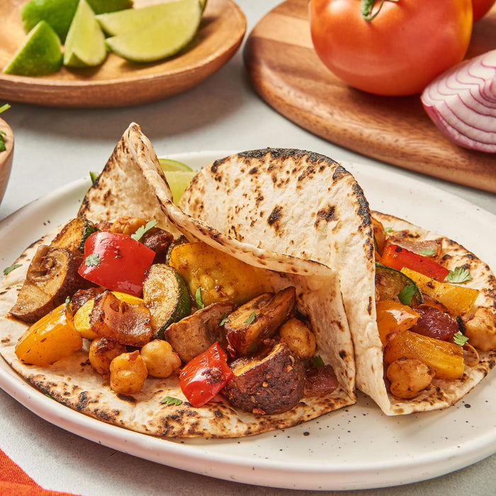 ['A plate of two tortillas filled with roasted vegetables and chickpeas.']