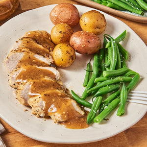 ['A plate of sliced chicken breast with gravy, green beans, and roasted potatoes.']