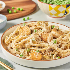 ['A plate of fettuccine pasta with peas, mushrooms, and scallops.']