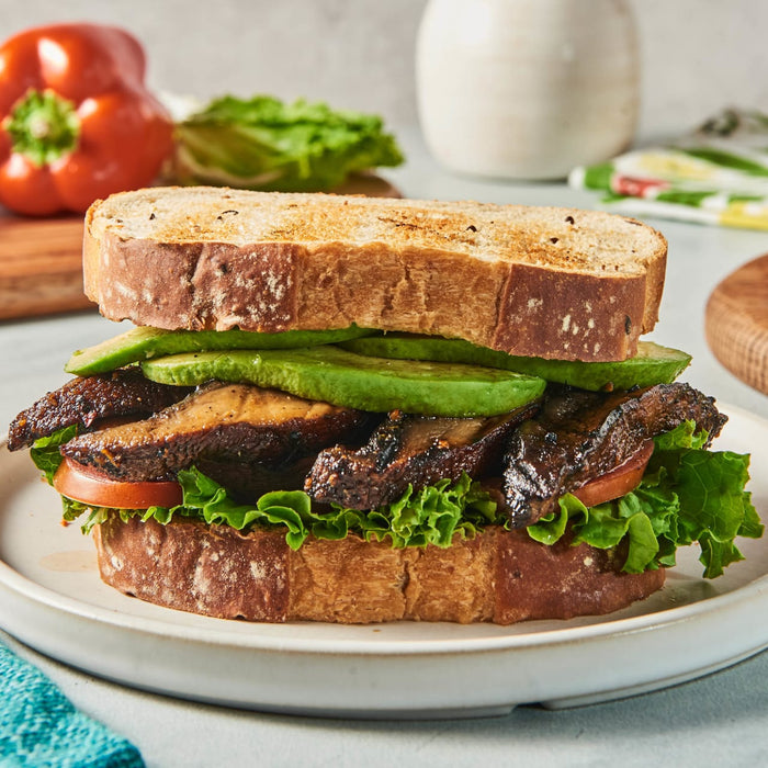 ['A sandwich with grilled mushrooms, avocado, lettuce, and tomato on toasted bread.']