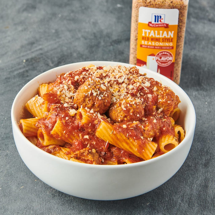 A bowl of pasta with meatballs and marinara sauce topped with parmesan cheese next to a McCormick Italian Red Wine Style Seasoning jar.
