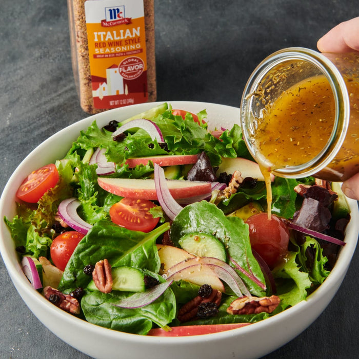A bowl of salad with red wine vinaigrette being poured on top with a McCormick Italian Red Wine Style Seasoning bottle in the background.