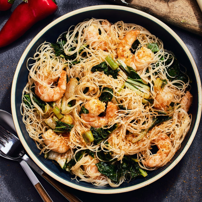 A bowl of rice noodles with shrimp bok choy and spices.