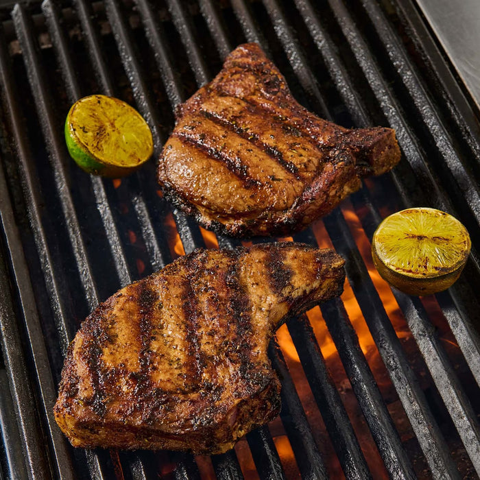 Two grilled pork chops with lime wedges on a grill with McCormick Grill Mates Chili Garlic Tri-Tip seasoning.