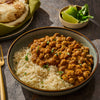 A bowl of chickpea curry served over rice with lime wedges and flatbread.