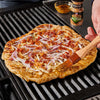 ['A close-up of a pizza topped with bacon, red onion, and cheese being brushed with McCormick Grill Mates Dill Pickle Seasoning on a grill.']