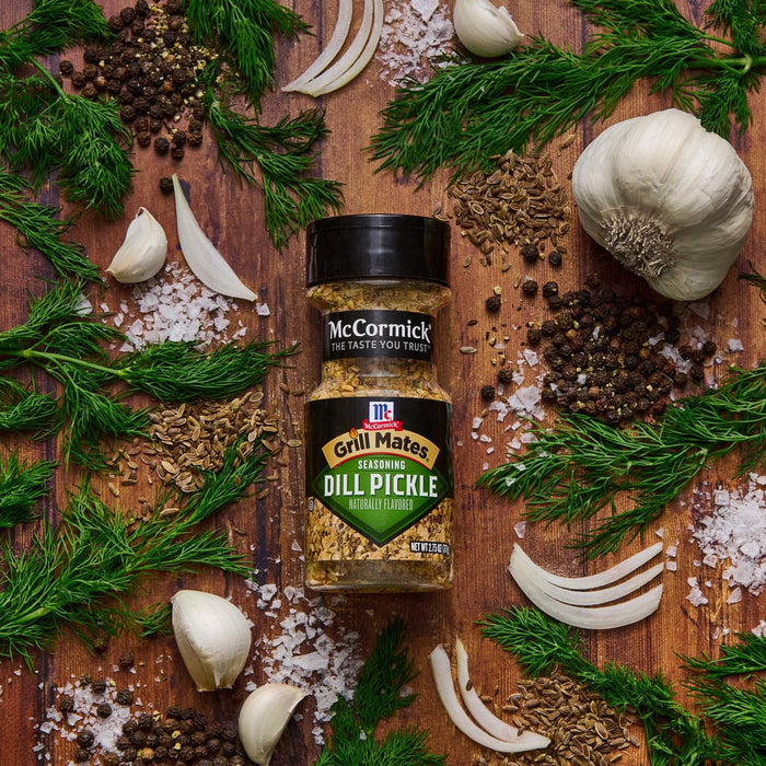 ['A jar of McCormick Grill Mates Dill Pickle seasoning is surrounded by dill, garlic, salt, and peppercorns.']